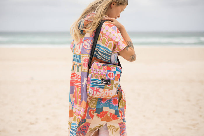 Colorful retro-patterned hooded towel with geometric and tropical prints, worn over shoulder at beach.