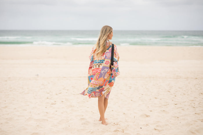 Retro Shores hooded towel in multicolored abstract print, worn on beach by woman facing ocean
