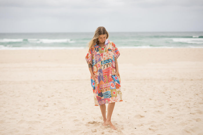 Colorful retro patterned hooded towel with geometric and abstract designs in coral, blue, and yellow, worn on beach.