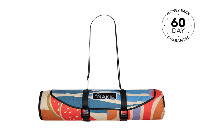 Rolled recycled picnic blanket with colorful retro fruit and stripe pattern, black carry straps and NAKIE logo label.