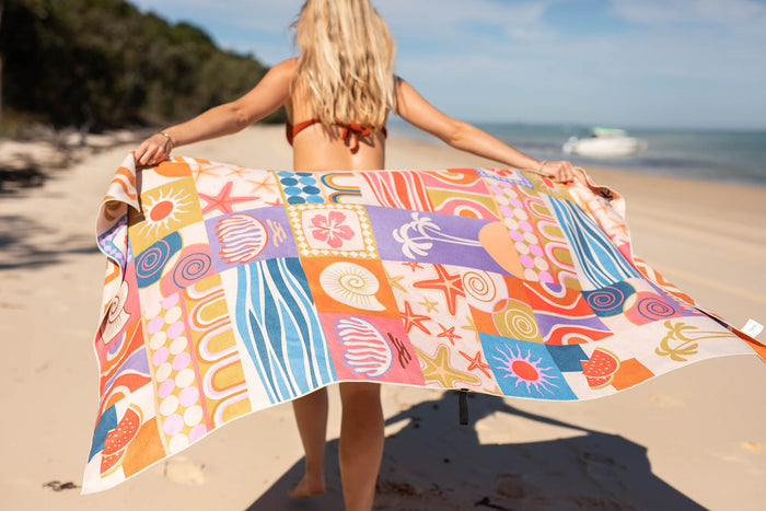 Colorful patchwork beach towel with retro sun, starfish, and geometric patterns in orange, blue, purple