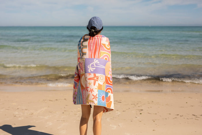 Recycled sand-free beach towel with retro multicolour coastal print, worn over shoulders at beach