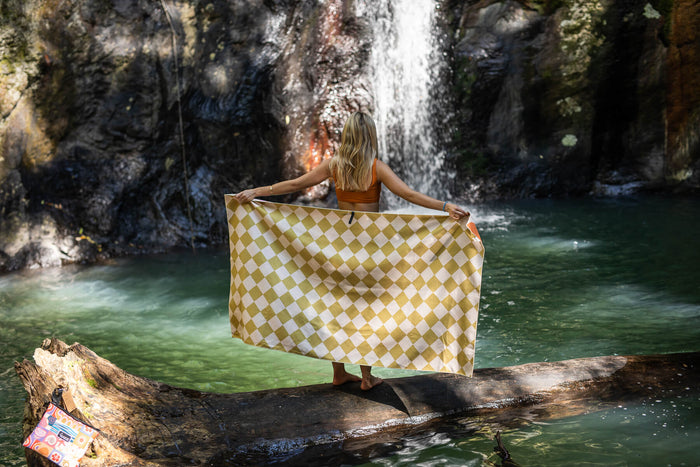 Gold and cream diamond-patterned recycled beach towel held open by woman at waterfall