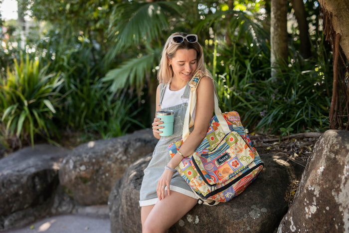 Retro Shores recycled tote bag with colorful beach-themed print, carried by woman in outdoor garden setting.