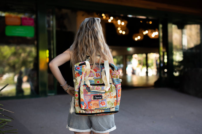 Colorful retro-print recycled tote bag with cream canvas handles, worn on back by person in urban setting.