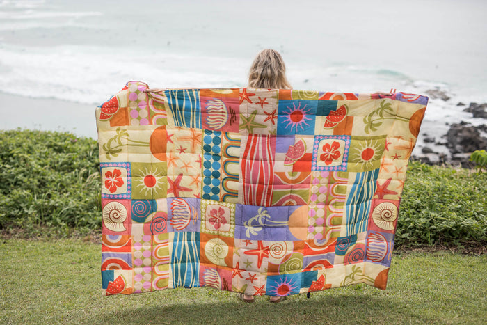 Retro Shores patchwork puffy blanket with colorful geometric and tropical print blocks, displayed outdoors by ocean.