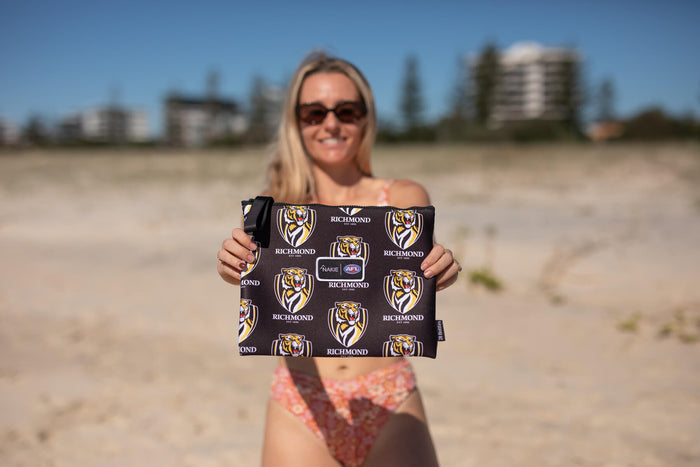 Black Richmond Tigers AFL recycled sand-free beach towel with tiger logo and text pattern, held up on beach