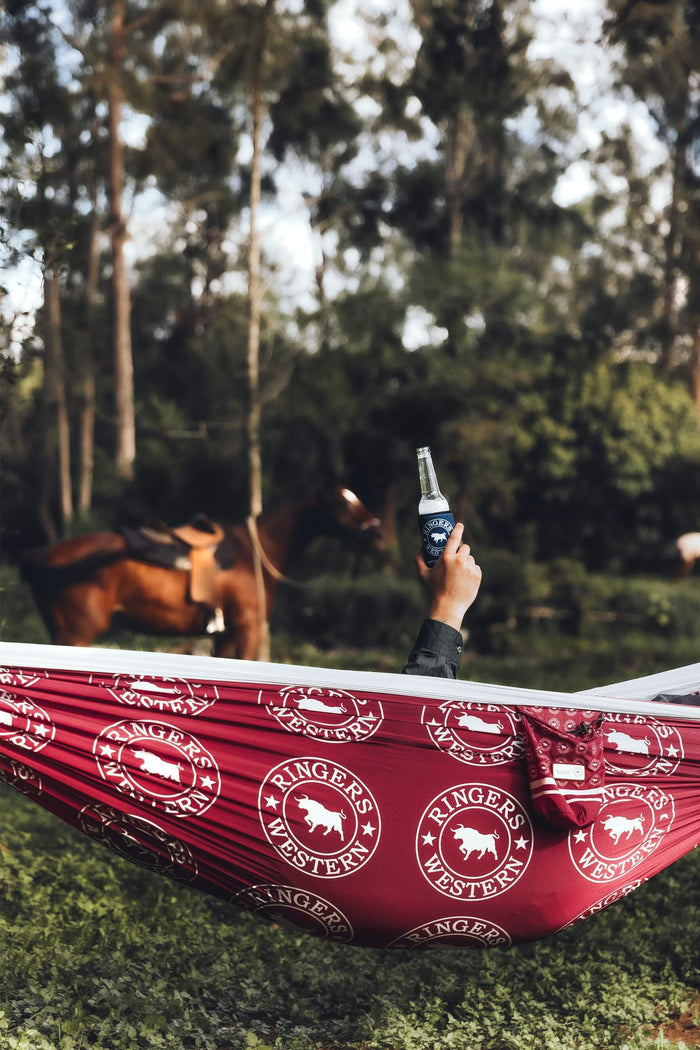 Red Ringers Western recycled hammock with white bull logo pattern, held aloft in forest setting with straps visible