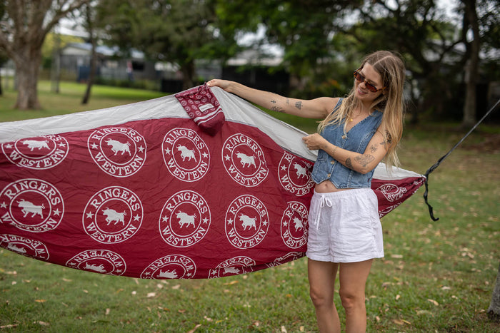 Ringers Western burgundy hammock with repeating bull logo and white trim, displayed outdoors in park setting