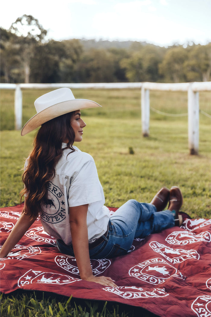 Ringers Western recycled picnic blanket in burgundy with cream logo pattern, displayed on grass field