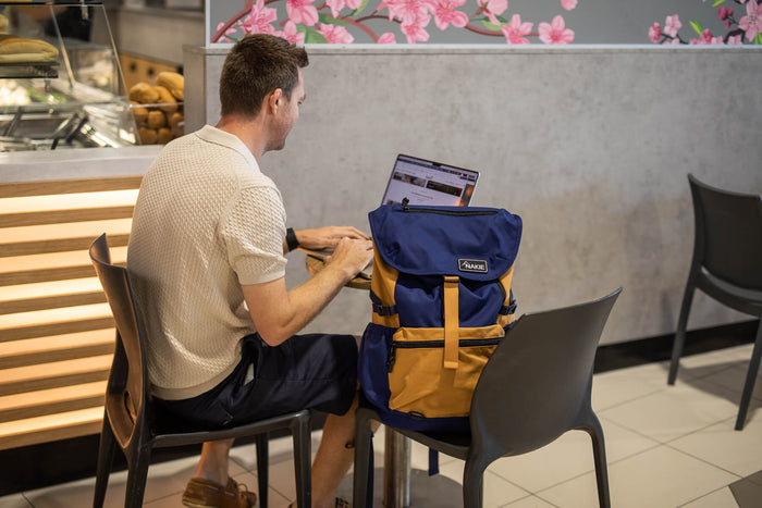 Navy and mustard recycled travel backpack with laptop compartment, shown open with laptop inside on user's lap.