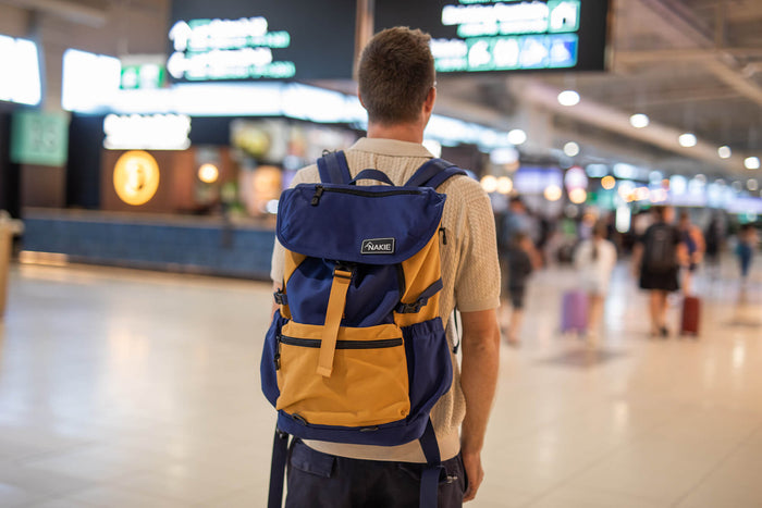 Navy and gold colorblock recycled travel backpack with flap top and padded straps, worn in airport.