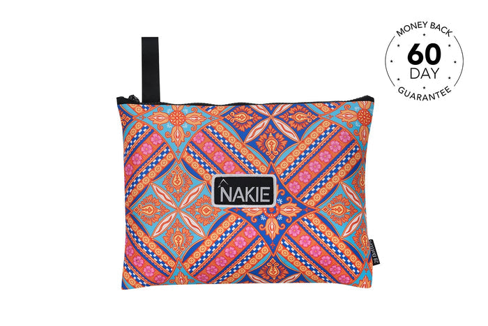 Colorful geometric patterned beach towel in blue, orange, and pink with black carry handle and NAKIE logo label.