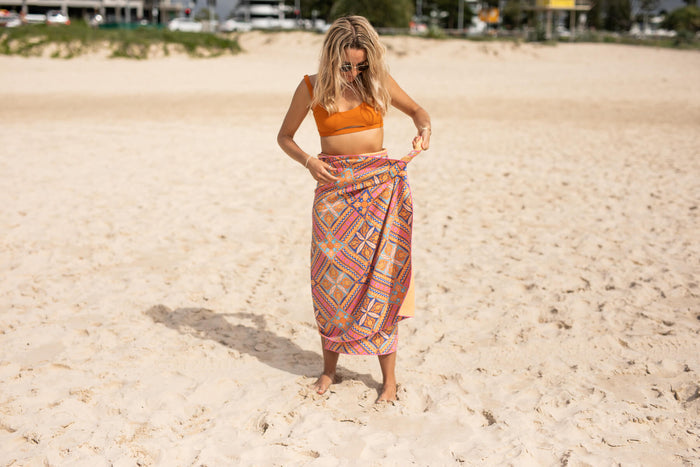 Recycled sand-free beach towel in coral geometric print, worn as wrap on beach