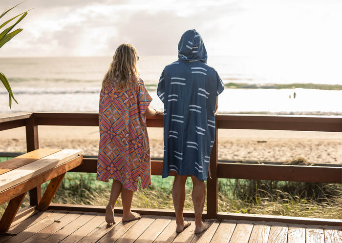 Navy hooded towel with striped pattern worn over shoulders at beach by child, shown from back view