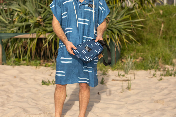 Blue hooded towel with white geometric stripe pattern, worn on beach with matching navy crossbody bag visible