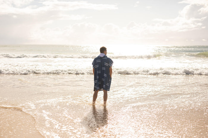 Navy stripe hooded towel with white dashes worn by child wading in ocean waves.