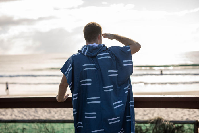 Navy hooded towel with light blue horizontal stripes, worn by person at beach, rear view