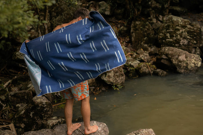 Navy beach towel with white geometric dash pattern, shown on child by water's edge