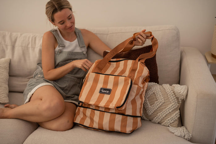 Sandy Trails recycled tote bag in tan and cream stripes with black trim and handles, displayed open on a sofa.