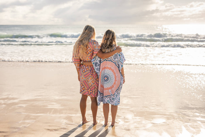 Two women wearing patterned hooded towels standing in ocean shallow water at beach