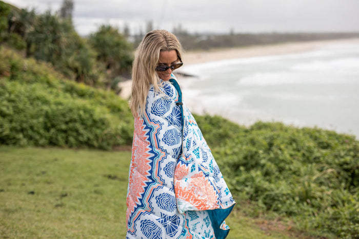 Sustainable down puffy blanket with blue, coral, and white geometric pattern, draped over shoulder outdoors.