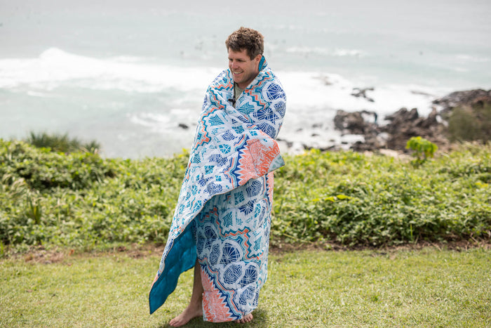 Sustainable down puffy blanket with blue and orange geometric print, wrapped around man at beach