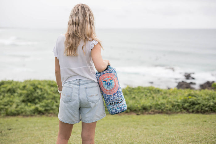 Sustainable down puffy blanket with coral and blue mandala pattern, shown rolled and carried over shoulder outdoors