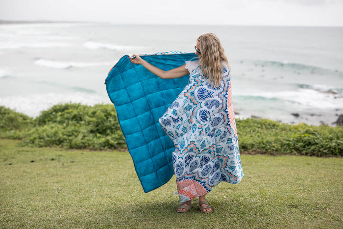 Bright turquoise quilted puffy blanket displayed outdoors with geometric patterned kimono at seaside.