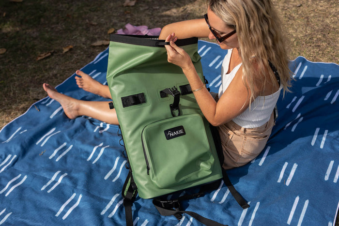 Spring green recycled cooler backpack with black straps and buckles, displayed open by person sitting outdoors.