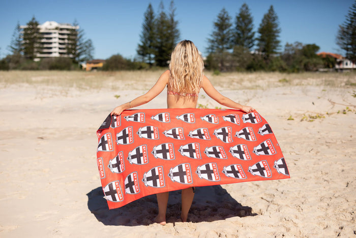 Red AFL beach towel with repeating St Kilda Saints logo pattern, held by woman on sandy beach