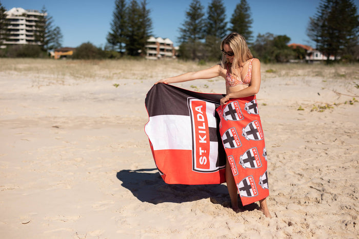 St Kilda Saints red, white and black beach towel with logo print, held on sandy beach