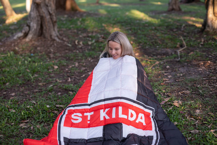 St Kilda Saints red, white and black quilted puffy blanket draped over person outdoors.