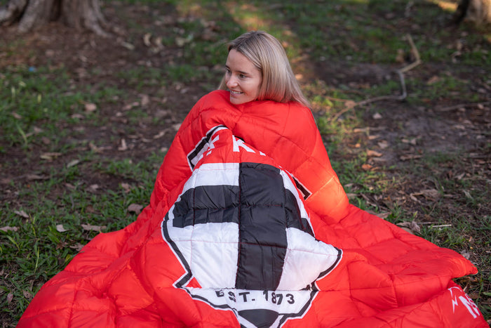 Red quilted puffy blanket with St Kilda Saints AFL logo and black-and-white checkered shield design, draped over person outdo