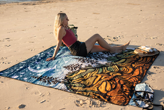 Recycled picnic blanket with blue starry night and orange butterfly wing patterns, spread on sand beach.