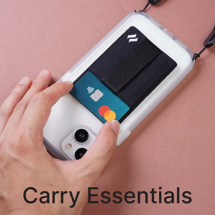 A hand inserts a teal Mastercard into a black Stick On Wallet from Catalyst Case US, attached to the back of a white phone case resting on a pink surface. The wallet is part of the Stick On Wallet & Shoulder Strap Bundle.