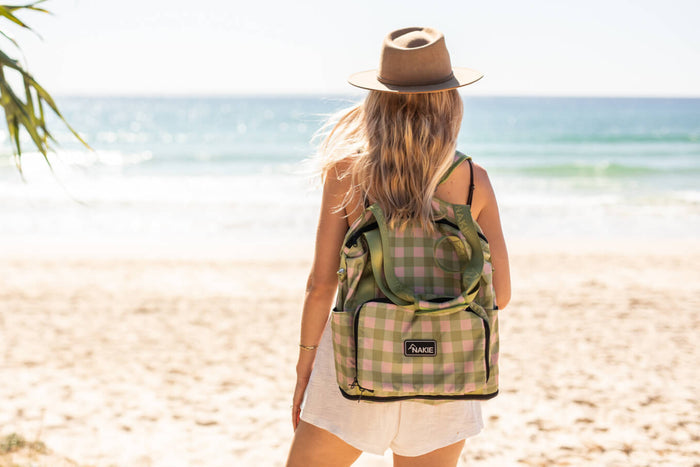 Green and pink gingham recycled tote bag with black trim, worn as backpack on person at beach
