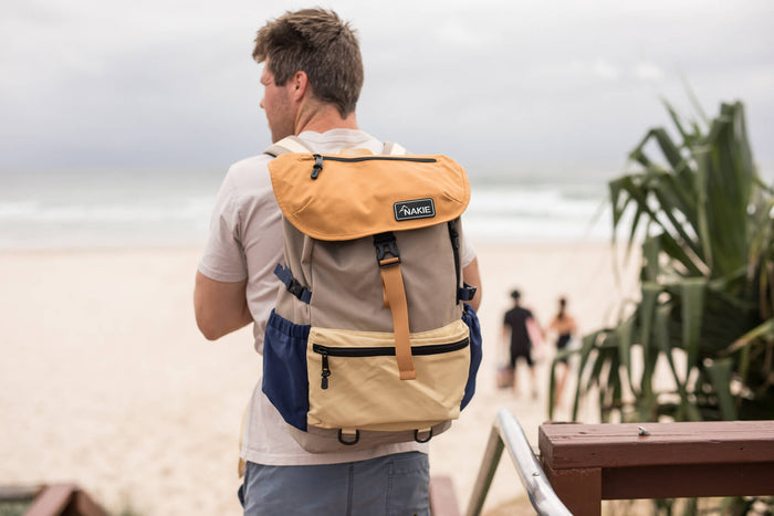 Tan and navy colorblock recycled travel backpack with tan leather straps, worn by man at beach