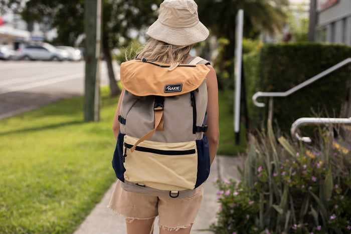 Beige and navy colorblock recycled travel backpack with tan flap, worn on back outdoors