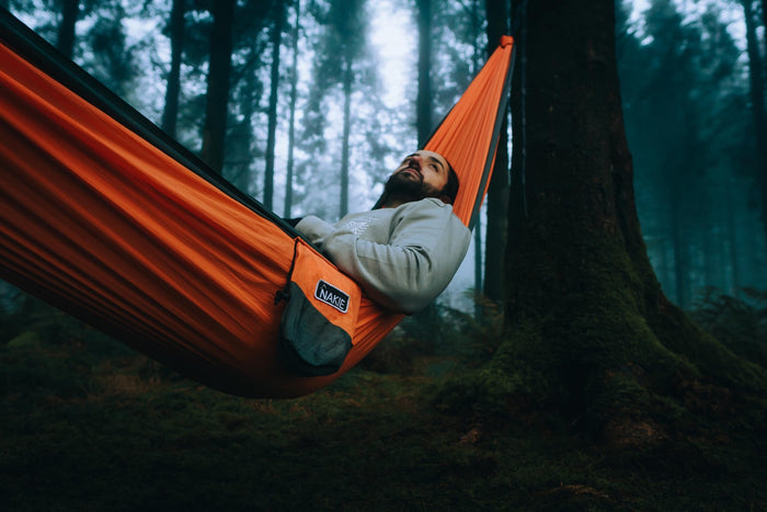 Sunburnt orange recycled hammock with integrated straps, suspended between trees in forest setting