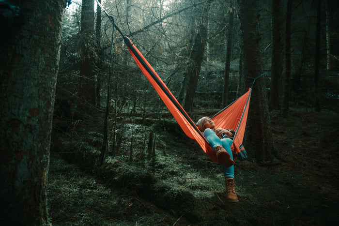 Sunburnt orange recycled hammock with straps suspended between trees in forest setting, person reclining inside.