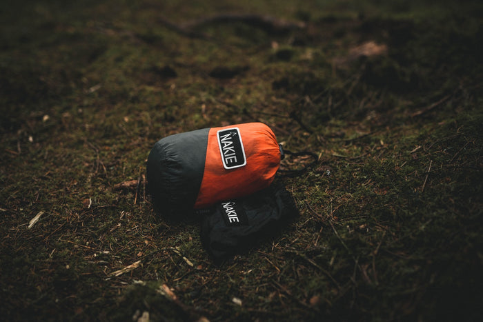 Sunburnt Orange recycled hammock with black straps, shown rolled and compressed in carry bag on forest ground.
