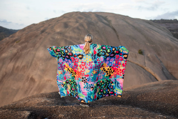 Colorful patchwork quilted blanket with leopard and abstract patterns worn as cape outdoors on mountain terrain