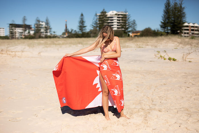 Sydney Swans red, white and navy beach towel with logo pattern, displayed on sand at beach