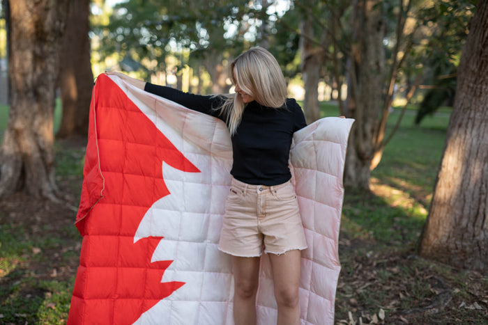 Red and white quilted down puffy blanket with maple leaf design, displayed outdoors by woman in black top and cream shorts