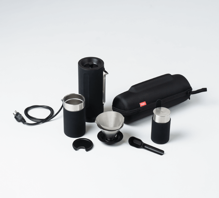 Portable travel coffee kit: grinder, metal filter, scoop, small cup, power cord, and zippered black case on white background