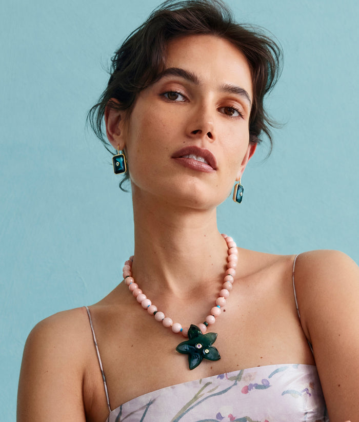 Model on grey backdrop wears strappy dress with Vinca Flower Necklace and Tile Earrings in Denim.