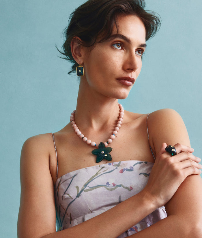 Model on grey backdrop wears strappy dress with Monument Ring, Vinca Flower Necklace, and Tile Earrings.