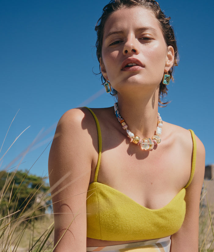 Model on dune grass wears yellow top with Tile Earrings and Glass Beach Necklace, alt view.