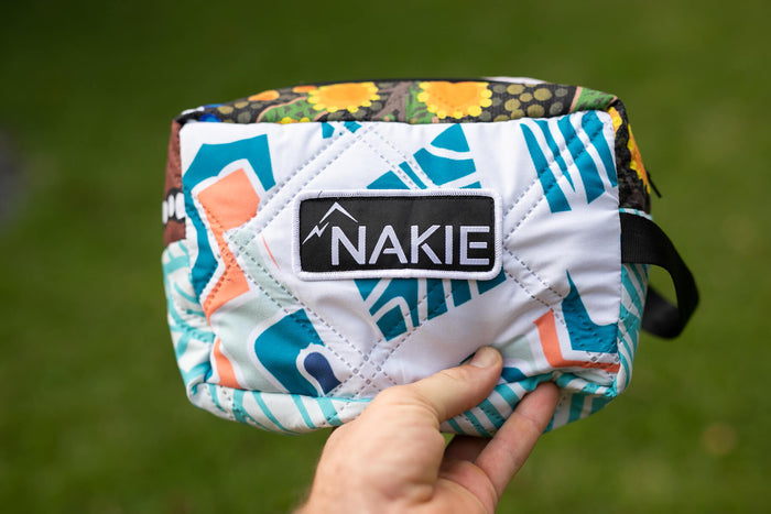 Nakie quilted toiletry bag with teal and coral geometric pattern, held in hand against green background